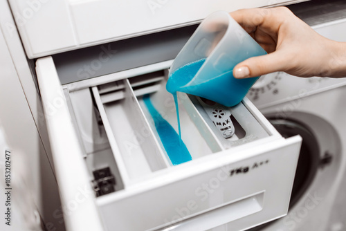 Photos Hand pouring blue liquid detergent into washing machine drawer, showcasing laund