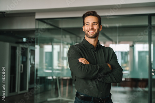 Corporate portrait of European confident student, trade manager businessman standing crossed arms in office. Young latin hispanic specialist business man employee smiling dreaming away. Copy space