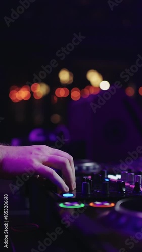 Close up of DJ hands adjusting mixer controls and performing live set on professional turntables with colorful club lights and blurred nightlife background
