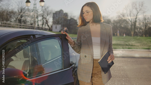 Woman standing next to a car with sunlight shining behind her in a park during the afternoon