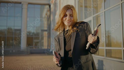 Woman enjoys music while dancing outside a modern building during sunset in an urban area