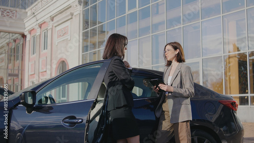 Business meeting between two women outside a building in a city during daylight with a parked car nearby
