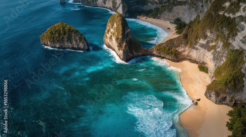 A beach is seen surrounded by high cliffs and large rock formations. Waves crash on the shore. The sun shines brightly on the blue water. This scene shows a tropical coastal area.