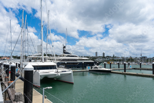 A collection of luxury yachts and motorboats moored at the bustling Viaduct Harbour with the modern Auckland CBD skyline in the background.