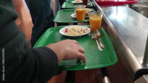 Customers slide trays along metal rails to select lunch dishes in a busy public dining room, showing a self-service cafeteria line and diverse meal options in high-quality 4k resolution.