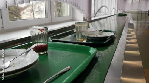 Dirty kitchen trays with leftovers move on a motorized conveyor belt toward the industrial washing area in a busy catering canteen, showcasing high-volume commercial dishwashing processes in 4k.