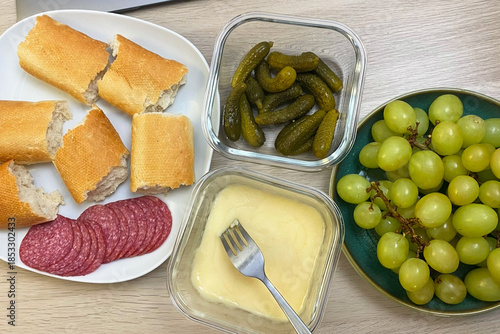 Appetizer Platter with Melted Cheese, Salami, Bread, Pickles, and Grapes