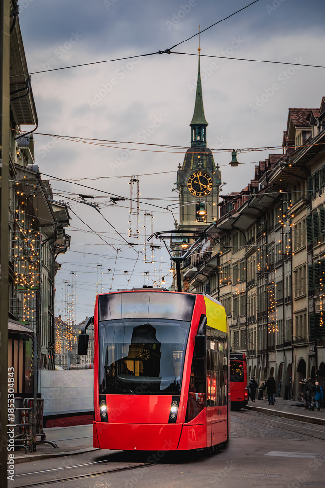 Fototapeta premium Red tram and arcades under festive lights in the Old Town Bern, Switzerland