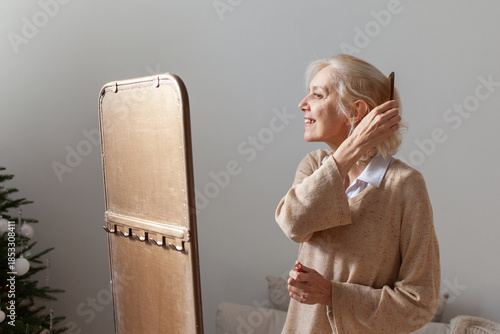 Photography elderly gray-haired woman combs her hair near mirror at home, her grandmother ta