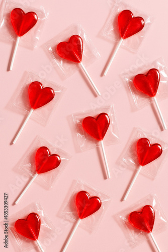 Heart shaped red lollipops on pink background. Playful Valentine’s Day candy pattern symbolizing love, sweetness and cheerful celebration