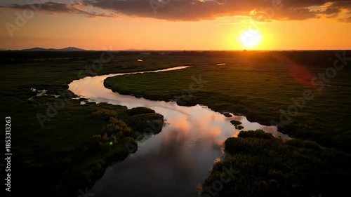 Serene winding river flows through lush green landscape at sunset with dramatic orange sky and clouds