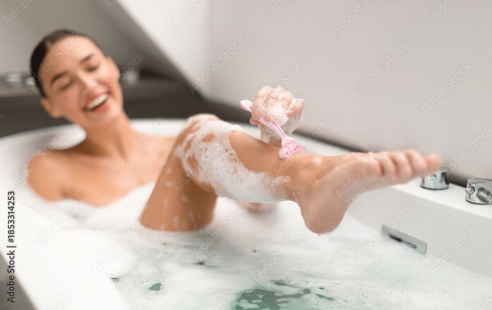 Fototapeta premium Body Hair Removal. Happy Woman Shaving Legs Using Safety Razor Caring For Herself Bathing In Modern Bathroom At Home. Depilation And Skincare Cosmetics Concept. Selective Focus