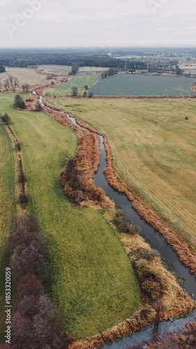 Cinematic vertical drone flight over the winding Barycz River near Gądkowice revealing the scenic Milicz Ponds landscape within the historic Carp Valley in Poland, Europe, under a moody, overcast wint