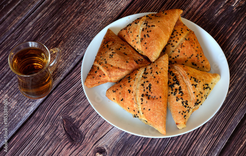 A plate with several fresh oriental meat buns samsa and a glass cup with tea on a wooden table.