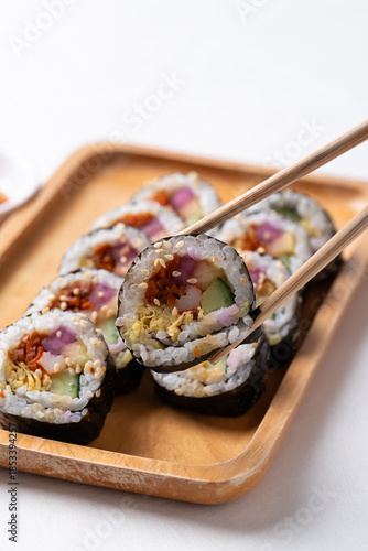 Kimbap or Gimbap, Korean food made from cooked rice with vegetables, egg and wrapped with dried seaweed on wooden plate eating by chopsticks