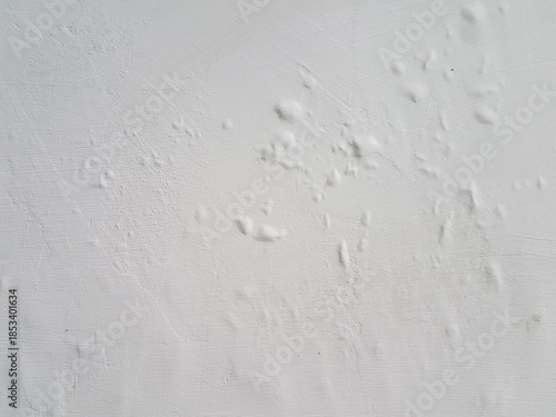 Detail of a white painted wall showing small blisters and bumps. Water damage and bubbling paint texture on a white interior wall. Abstract background of deteriorating paint and swollen plaster.