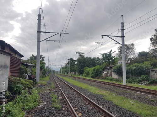 Double railway tracks extending toward the horizon. Utility poles stand beside the tracks under a cloudy sky. View of transportation