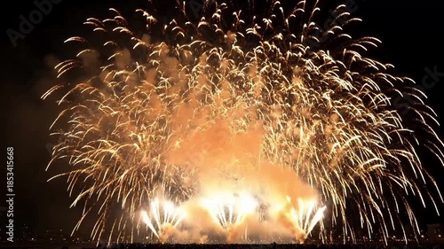 Spectacular golden fireworks display illuminates the dark night sky above a crowded gathering below