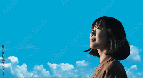 春・上を見上げ微笑む明るい表情の日本人女性の顔　前向きでポジティブ希望に満ちた表情　就職・新生活・旅行・リラックス・入学のイメージ　青空と雲の背景