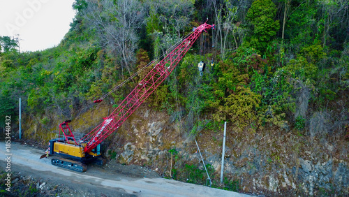 Crawler crane working on a mountain roadside slope.
Heavy construction machinery stabilizes a steep forested hillside during infrastructure work with visible cables, boom structure, and rugged terrain