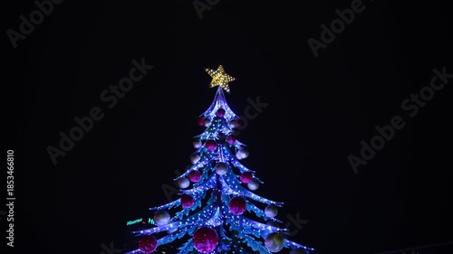 Christmas tree in a European city decorated with many glowing lights and a golden star on top, slowly rotating around its axis and creating a magical holiday fairy-tale atmosphere. Perfect for festive