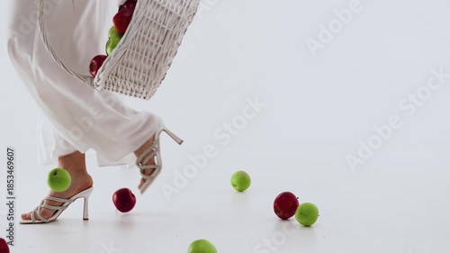 A woman in the studio is scattering apples from a basket on the floor