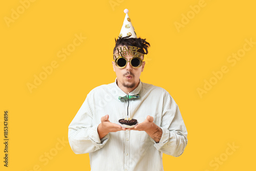 Happy young man with Birthday cake making wish on yellow background