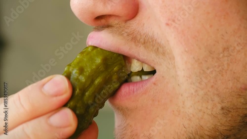 Extreme close up man mouth he bites into crunchy pickled gherkin, enjoying sour taste of fermented vegetable before chewing with satisfaction. Close up of man eating crispy dill pickle