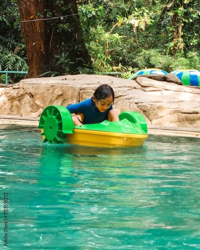 Little girl on a mini boat floating in the wate at a water park.