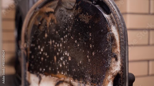 A sooty fireplace window is sprayed with cleaning agent