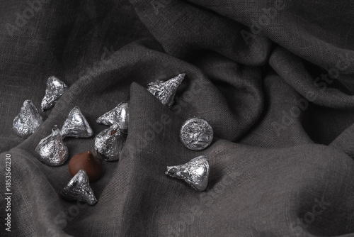 Minimalist gray background of soft linen fabric with beautiful folds and chocolates in silver wrappers.