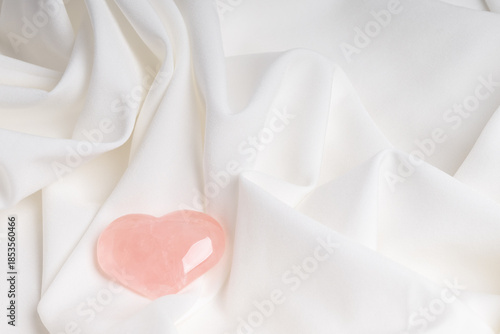 Minimalist composition on soft white fabric with a pink glass heart. Valentine's Day or birthday card.
