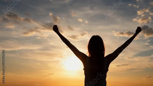 Empowered woman celebrates success with raised arms against a golden sunset sky