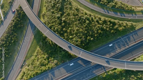 Aerial view of cars driving on a highway interchange in Manukau, Auckland, New Zealand. The roads are surrounded by green trees and grass. The scene shows transportation infrastructure.
