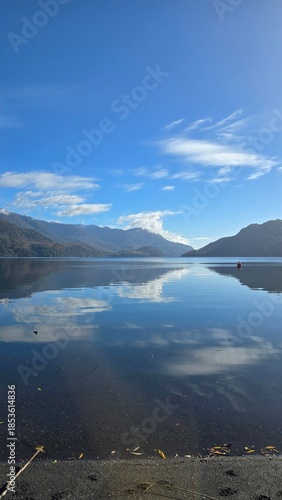 Scenic view of Choshuenco Lake on a sunny winter day in southern Chile. Calm waters surrounded by forested mountains, showcasing pristine nature and a peaceful Patagonian landscape.