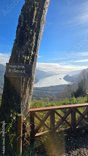 Winter landscape view from Mocho Choshuenco National Park on a cold, sunny day. A tree in the foreground frames forested mountains and a peaceful lake below, highlighting pristine nature in southern C