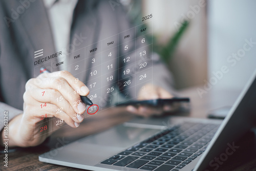 Businessman using stylus to circle December 31 on digital calendar overlay. Concept for year-end planning, project deadline, New Year resolution, and financial tax season scheduling on laptop.