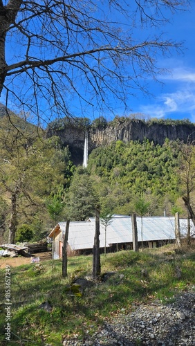 Big waterfall falling from a mountain, viewed from afar. Water cascades through lush green nature, creating a dramatic and peaceful landscape scene.