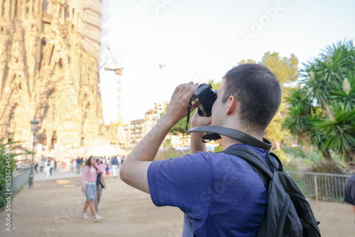 Cuadro en lienzo A man wearing a blue shirt and a black backpack is taking a picture of a large building