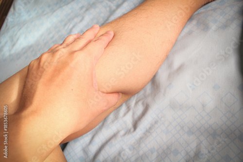 Close up of hand massaging leg on bed, concept of muscle pain relief, self-care and physical therapy at home.