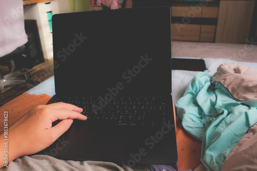 Close up of hand using laptop with blank black screen on bed at home.