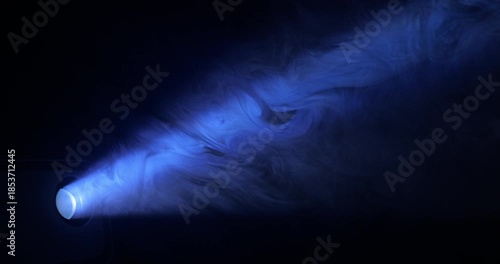 Blue Spotlight Beam Through Haze. Projector light ray piercing atmospheric smoke, building dramatic volumetric glow against dark background.
