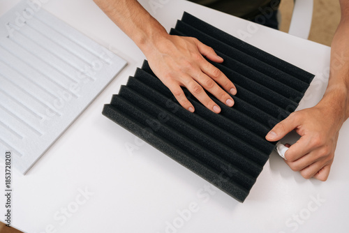 High-angle view of man checking soundproof foam panel doing quality check before installing acoustic insulation, preparing for diy project to improve audio quality and reduce noise for home recording.