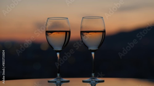 Two glasses filled with white wine standing at table, evening twilight, blurred background. Light alcohol for two persons standing ready, dim city and dusk sky on background
