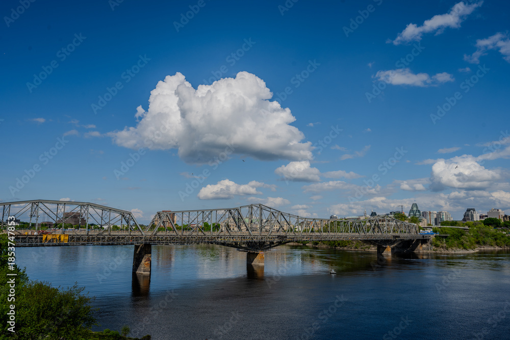 Obraz premium Steel truss bridge over river under blue sky with clouds
