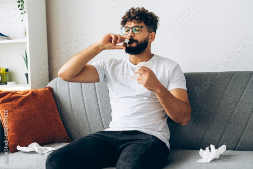 Photos Sad middle eastern man using nasal spray for allergy treatment at home sitting o