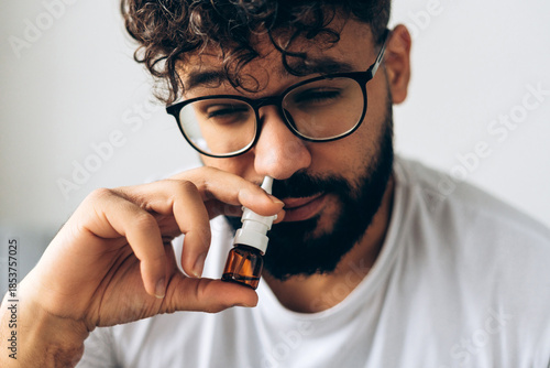 Sick, sad middle eastern man using nasal spray for cold and allergy relief closeup