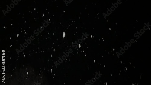 thick snow falls at night in the light of a streetlamp, snowflakes swirl in the wind and rush away against a black background.