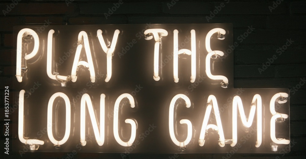 Fototapeta premium Bright neon sign displays text. Words play long game illuminate dark brick wall. Simple message, warm glow.