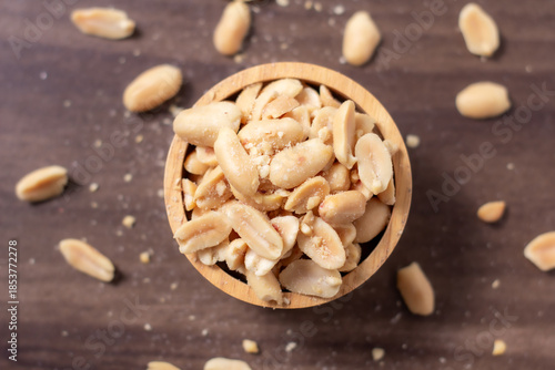 Peanuts in a wooden cup rest on a natural wood floor, creating a warm and rustic food-themed scene.